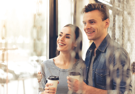 Beautiful young couple is holding a cup of coffee, looking out the window and smilingの写真素材