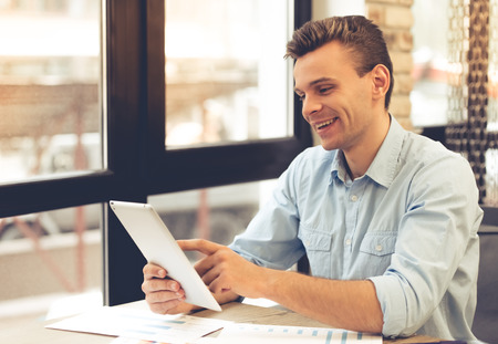 Handsome young businessman is using a digital tablet and smiling while working in officeの写真素材
