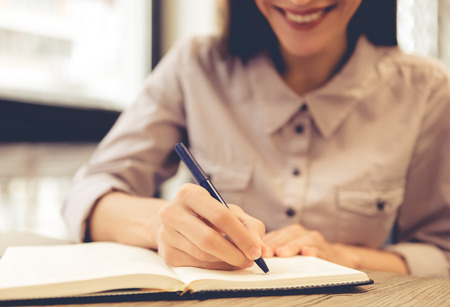 Cropped image of beautiful young business woman writing in her notebook and smiling while working in officeの写真素材