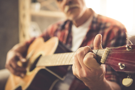 Cropped image of handsome mature man in casual clothes playing guitar at homeの写真素材