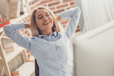 Beautiful business lady in formal shirt is holding hands behind head and smiling while working in the officeの写真素材