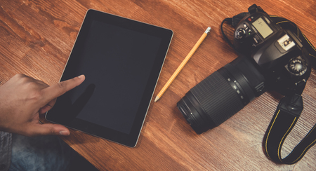 Cropped image of Afro American photographer using a digital tablet, his camera lying nearの写真素材
