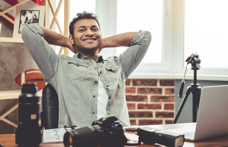 Attractive Afro American photographer is resting and smiling while sitting in his officeの写真素材