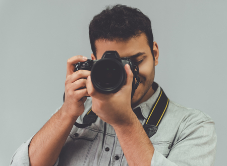 Attractive Afro American photographer is using his camera, on gray backgroundの写真素材