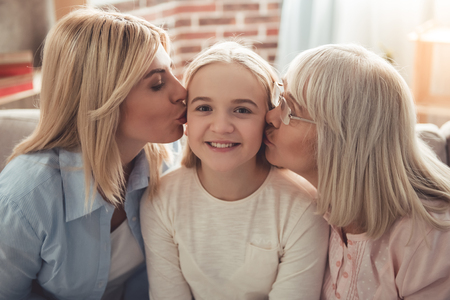 Three generations of women. Beautiful granny and mother are kissing teenage girl while sitting on...