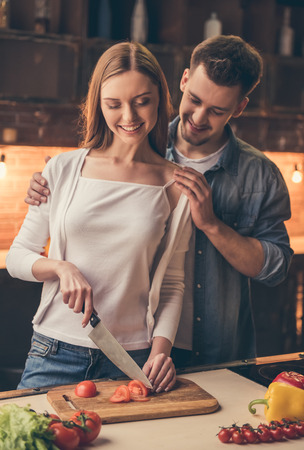 Beautiful couple is smiling while cooking together in the kitchenの写真素材
