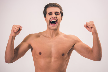 Portrait of handsome young naked man screaming, on gray backgroundの写真素材