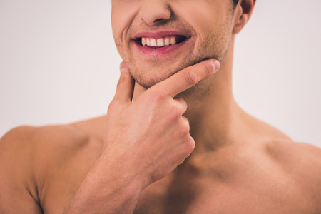 Cropped image of handsome young naked man touching his chin, on gray backgroundの写真素材