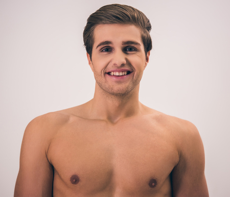Portrait of handsome young naked man looking at camera and smiling, on gray backgroundの写真素材