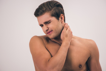Portrait of handsome young naked man feeling pain in his neck, on gray backgroundの写真素材