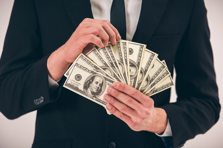 Cropped image of handsome young man in suit holding money, on gray backgroundの写真素材