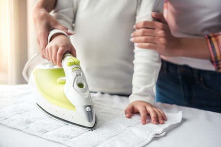 Cropped image of beautiful young woman and her little daughter ironing linenの写真素材