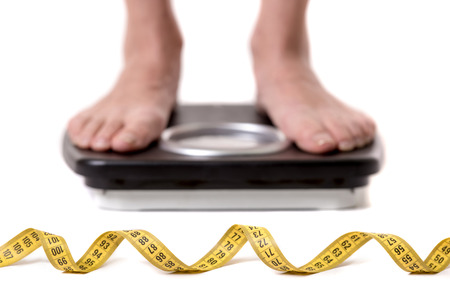 Cropped image of women feet standing on weigh scales, isolated on white. A tape measure in the foregroundの写真素材