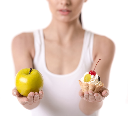 Healthy nutrition. Cropped image of girl holding a cake and an apple, isolated on whiteの写真素材