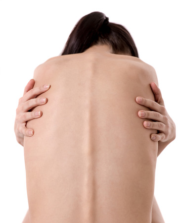 Back view of very thin girl with her arms wrapped about her torso, isolated on whiteの写真素材