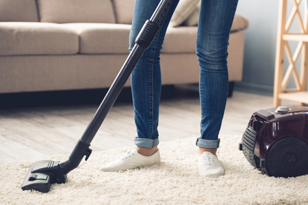 Cropped image of woman in jeans using a vacuum cleaner while cleaning her houseの写真素材