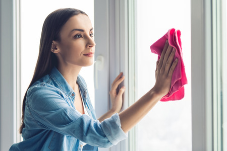 Beautiful young woman is using a rag while cleaning windowsの写真素材