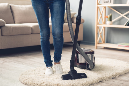 Cropped image of woman in jeans using a vacuum cleaner while cleaning her houseの写真素材