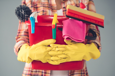 Cropped image of beautiful young woman in protective gloves holding a bucket with things for cleaning, on gray backgroundの写真素材