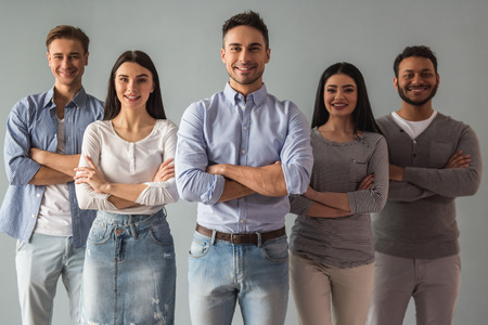 Beautiful young people in casual clothes are looking at camera and smiling while standing with...
