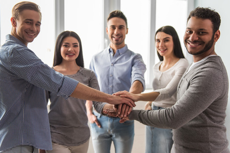 Group of beautiful young people in casual clothes are putting hands together and smiling
