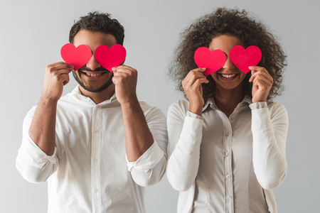 Beautiful Afro American couple is holding red paper hearts and smiling, on gray backgroundの写真素材