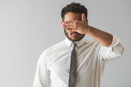 Handsome Afro American businessman in suit is covering his eyes, on gray backgroundの写真素材