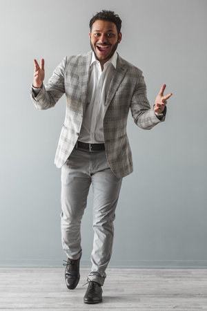 Full length portrait of stylish Afro American guy in gray suit looking at camera and smiling, on gray backgroundの写真素材