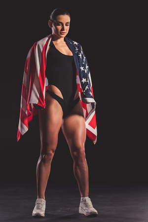 Full length portrait of beautiful strong muscular woman with American flag on dark backgroundの写真素材