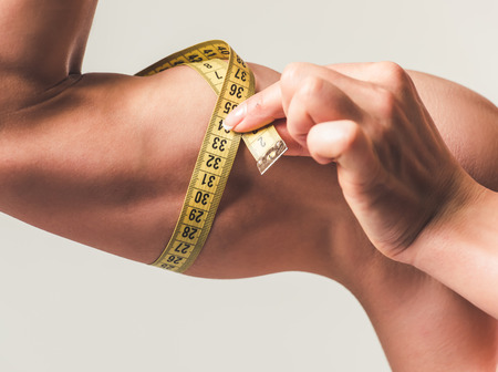 Cropped image of beautiful strong woman measuring her biceps, on light backgroundの写真素材