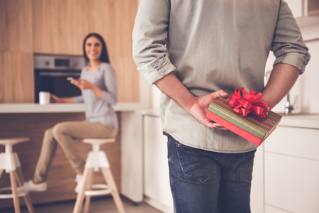 Rear view of man holding a gift box behind his back, his wife is smiling in the backgroundの写真素材