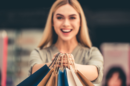 Attractive girl is holding shopping bags, looking at camera and smiling while standing in the mallの写真素材