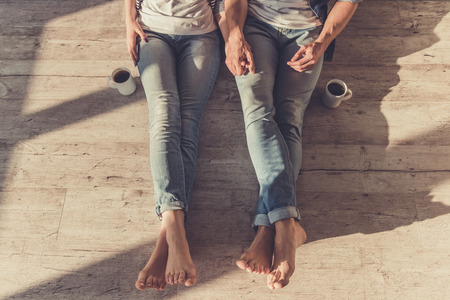 Cropped image of beautiful young couple holding hands while sitting on the floorの写真素材
