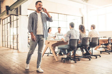 Successful young business people are working with laptops in business center. Guy is talking on the mobile phone and smilingの写真素材