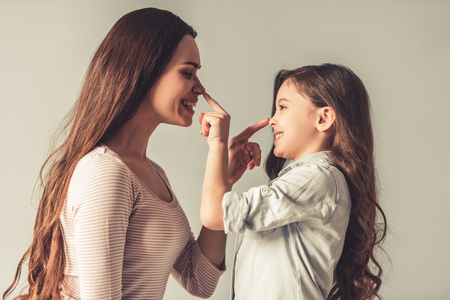 Charming little girl and her beautiful young mom are touching each others noses and smiling, on gray backgroundの写真素材