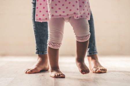 Afro American mom and her cute baby girl's legs, barefoot, on wooden floorの写真素材