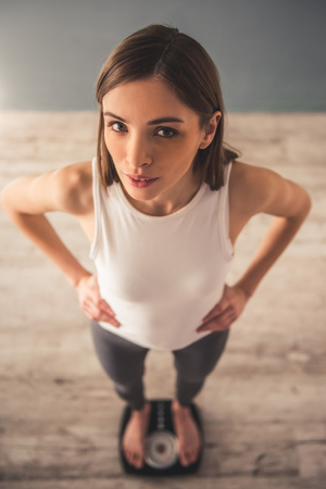 High angle view of girl standing on weigh scales and looking at cameraの写真素材