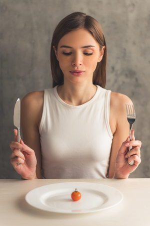 Eating disorder. Girl is sitting in front of the plate with a tomato and looking at itの写真素材