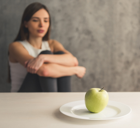 Eating disorder. Girl is sitting in front of the plate with an apple, fruit in focusの写真素材