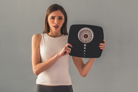 Girl is holding weigh scales and looking at camera, on gray backgroundの写真素材