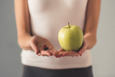 Eating disorder. Cropped image of girl holding an apple and pillsの写真素材