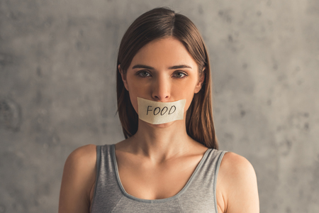 Suffering from anorexia. Girl is looking at camera, her mouth is sticked up with a word Food