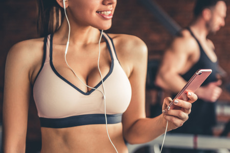 Attractive girl in earphones is smiling while running on a treadmill in gymの写真素材