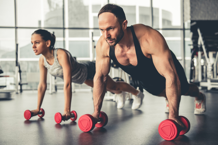 Attractive sports people are working out with dumbbells in gymの写真素材