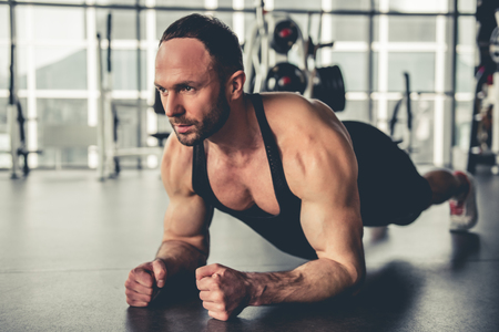 Handsome muscular man is doing plank exercise while working out in gym