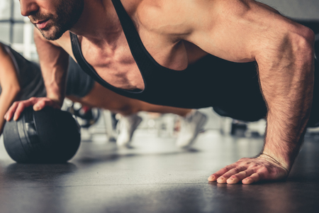 Attractive sports people are doing push-ups with fitness balls in gymの写真素材