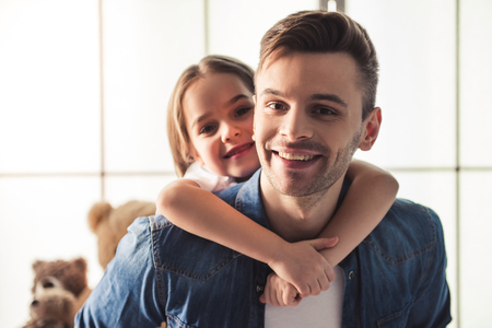 Charming little girl and her handsome young dad are hugging, looking at camera and smilingの写真素材