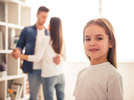 Charming little girl is looking at camera and smiling while her parents are dancing in the backgroundの写真素材