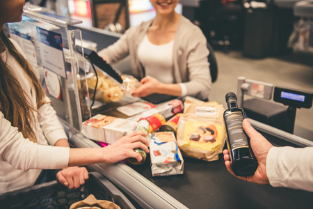 Dad and daughter at the cash desk in supermarket, beautiful cashier is smilingの写真素材