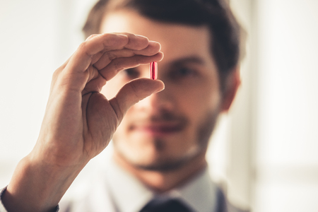 Handsome young doctor in white coat is holding a pill, hand with medicine in focusの写真素材